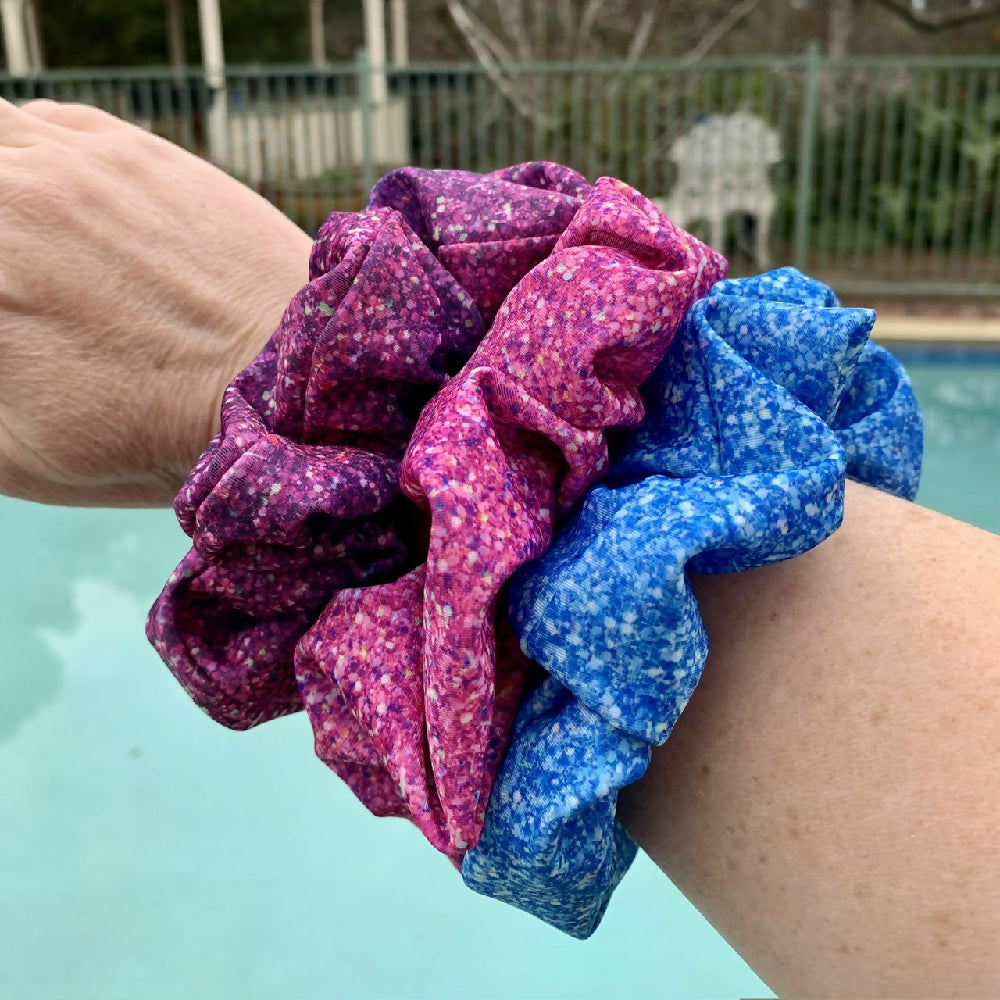 Purple, Pink & Blue Sparkle Swim Scrunchies on my arm with pool in background