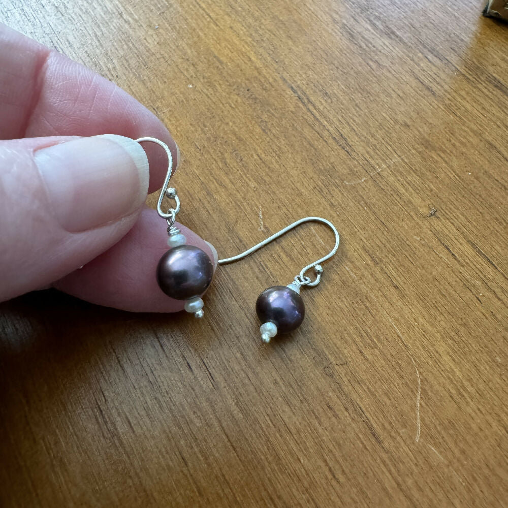 Large black pearl with 2 small white fresh water pearl earrings on wood background one hand held