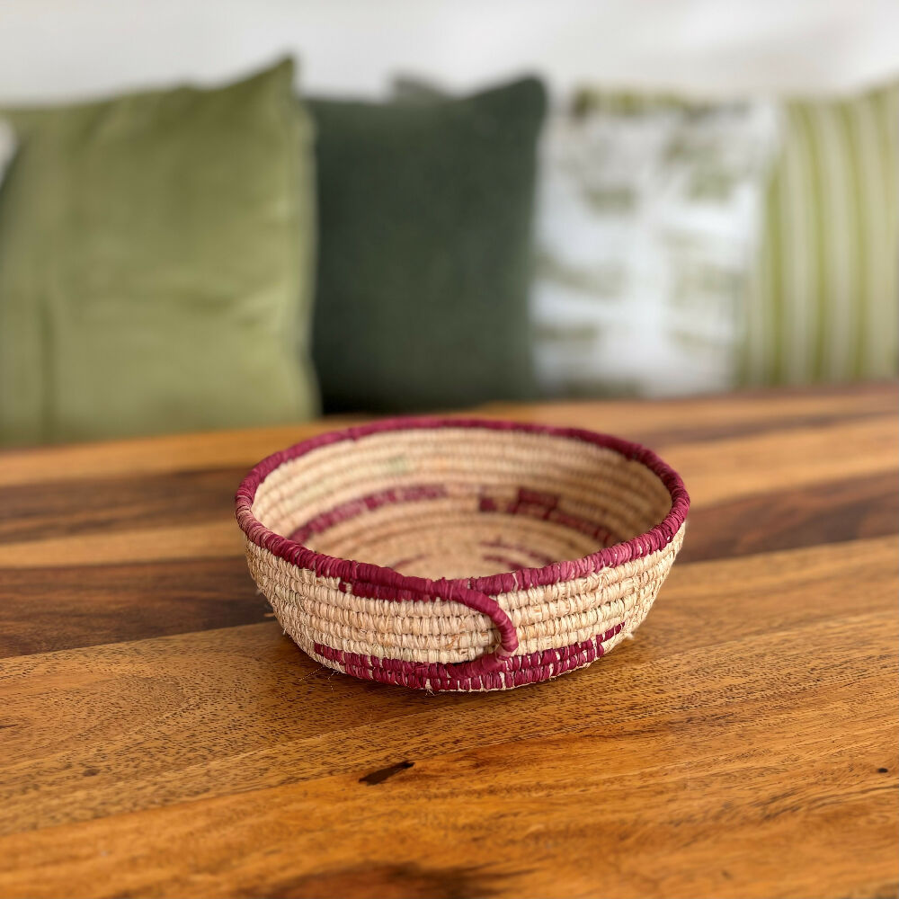 Handcrafted raffia bowl with red accents.