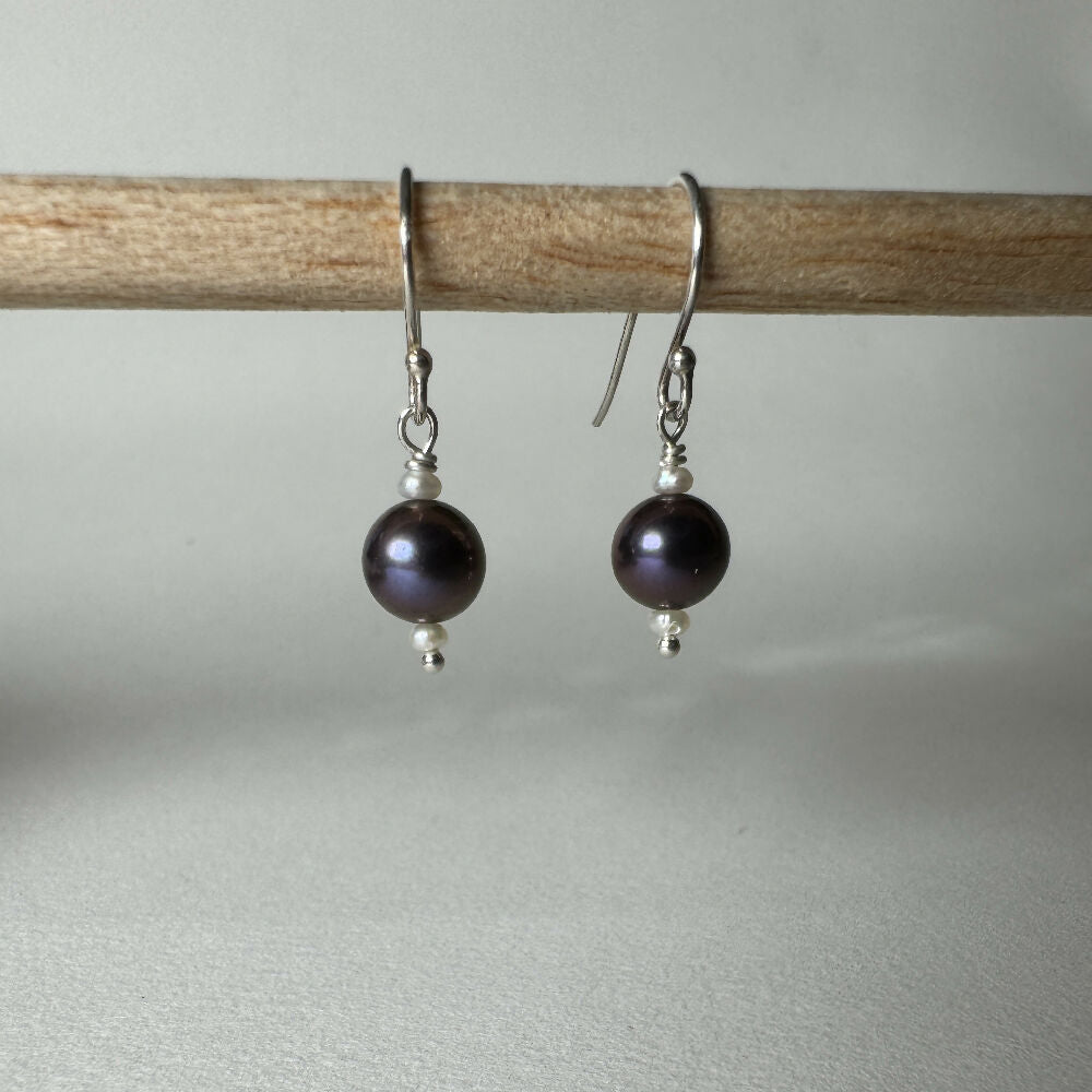 Large black pearl with 2 small white fresh water pearl earrings hanging on white background