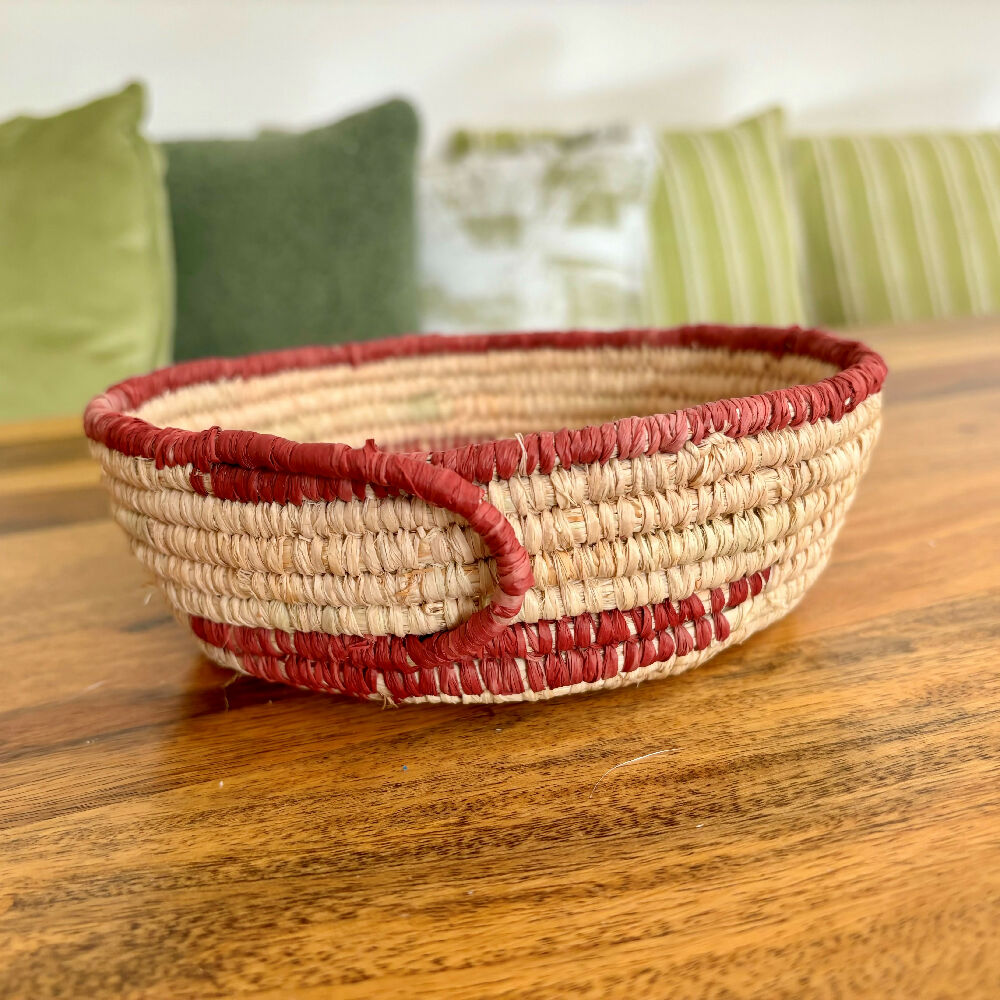 Handcrafted raffia bowl with red accents.