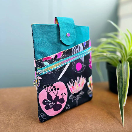 Book sleeve. Teal with native plants in rainbow colours.
