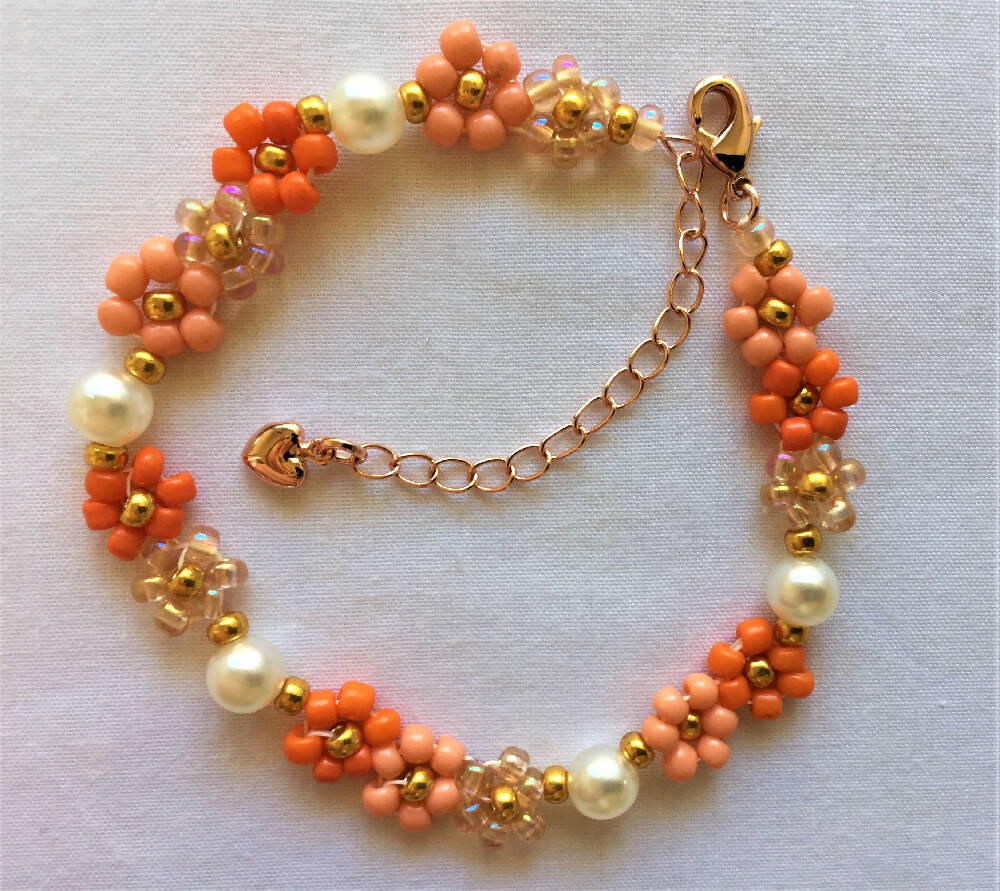 Naryanabeads faux pearls/orange daisy flowers bracelet made of beige faux pearls , daisy flowers of peach transparent, peach, golden and coral colour seed beads.