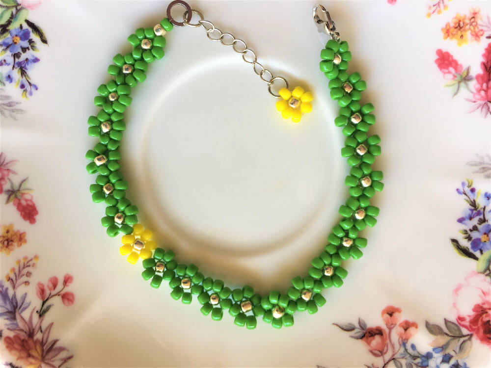 Naryanabeads green beaded bracelet made of green, yellow and golden colour seed beads. Clasp and extender chain - metallic silver colour, on the extender chain end yellow seed bead daisy flower