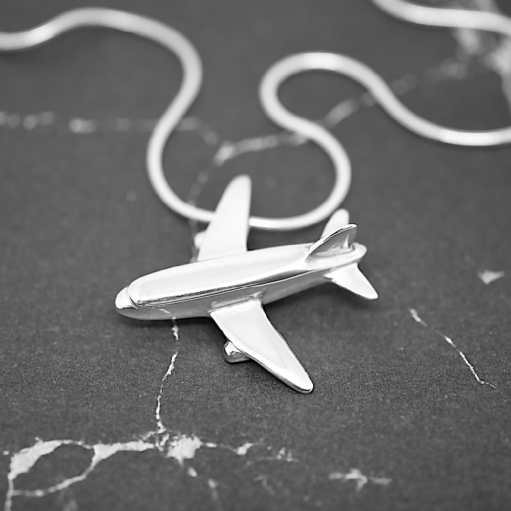 Image of handmade shiny sterling silver Aeroplane shaped pendant by Purplefish Designs Jewellery on silver snake chain necklace on a grey marble background.