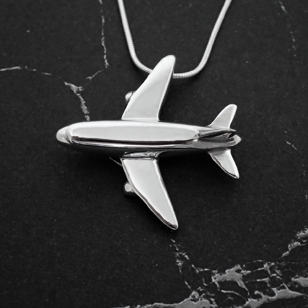 Image of handmade shiny sterling silver Aeroplane shaped pendant by Purplefish Designs Jewellery on silver snake chain necklace on a grey marble background.