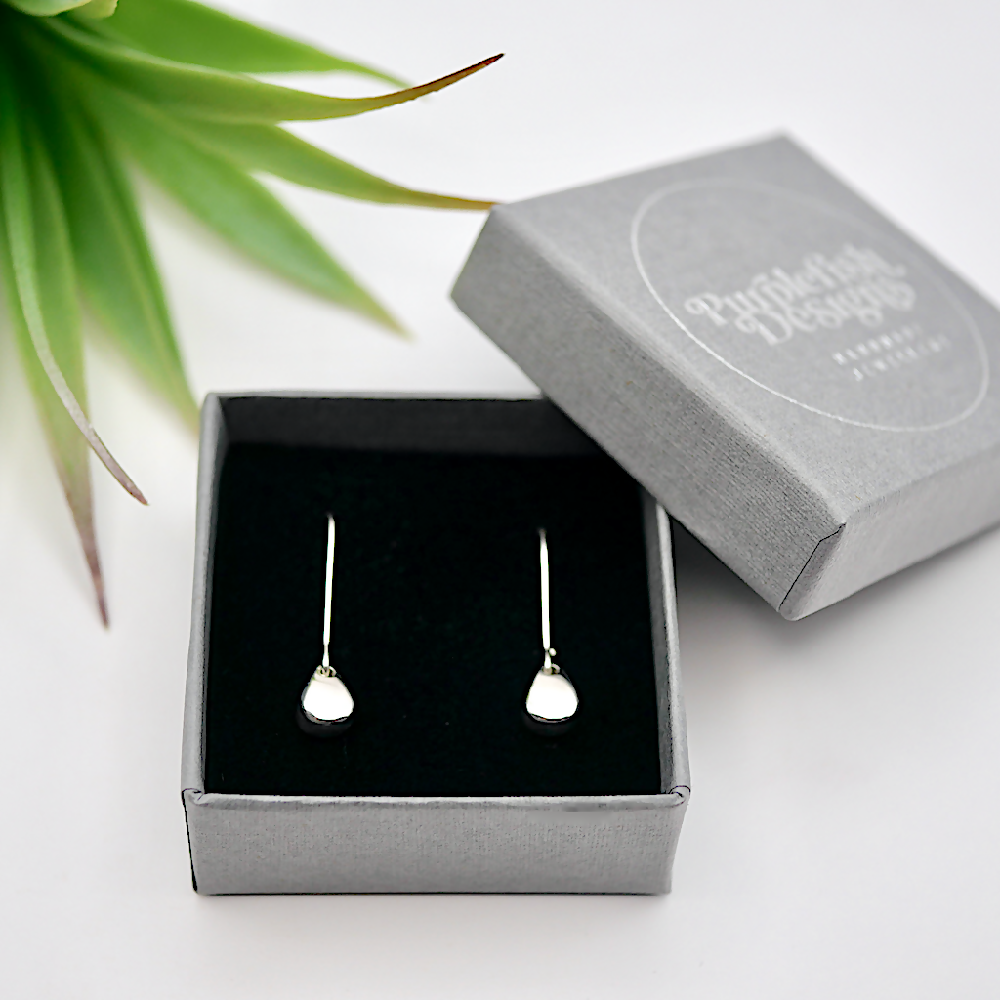 Image of a pair of sterling silver egg shaped earrings in a small grey jewellery gift box embossed with silver Purplefish Designs Handmade Jewellery logo. Box is on a white background with a decorative green plant.