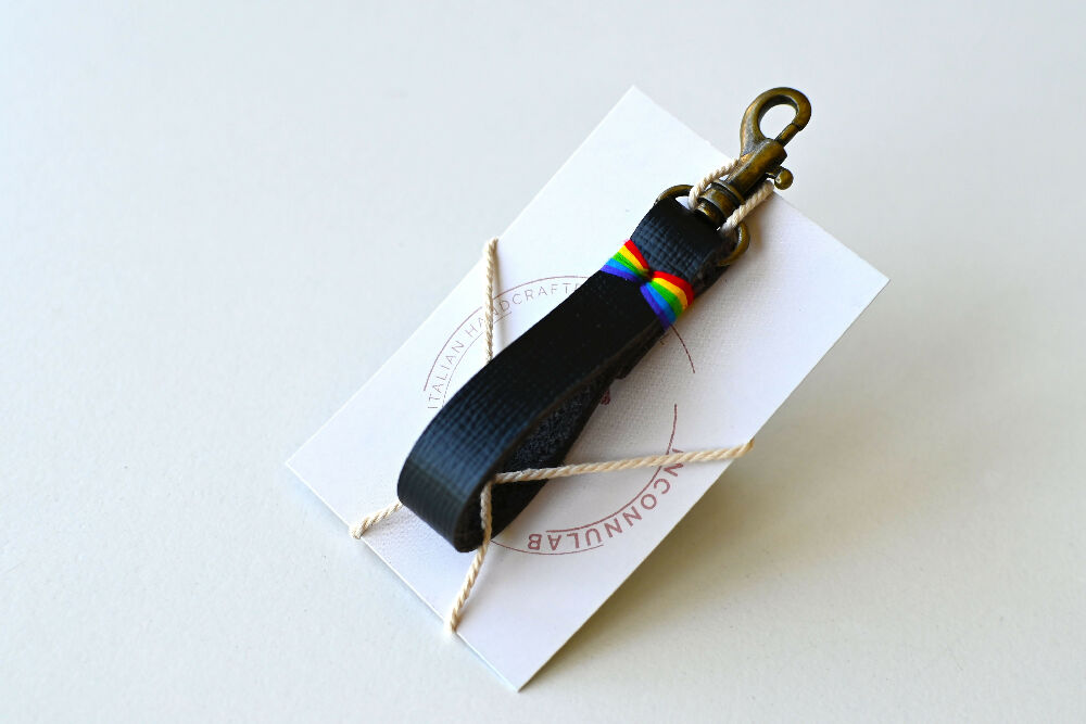A black keychain with colourful rainbow stitches is tied to a card. It has a brass snap hook.