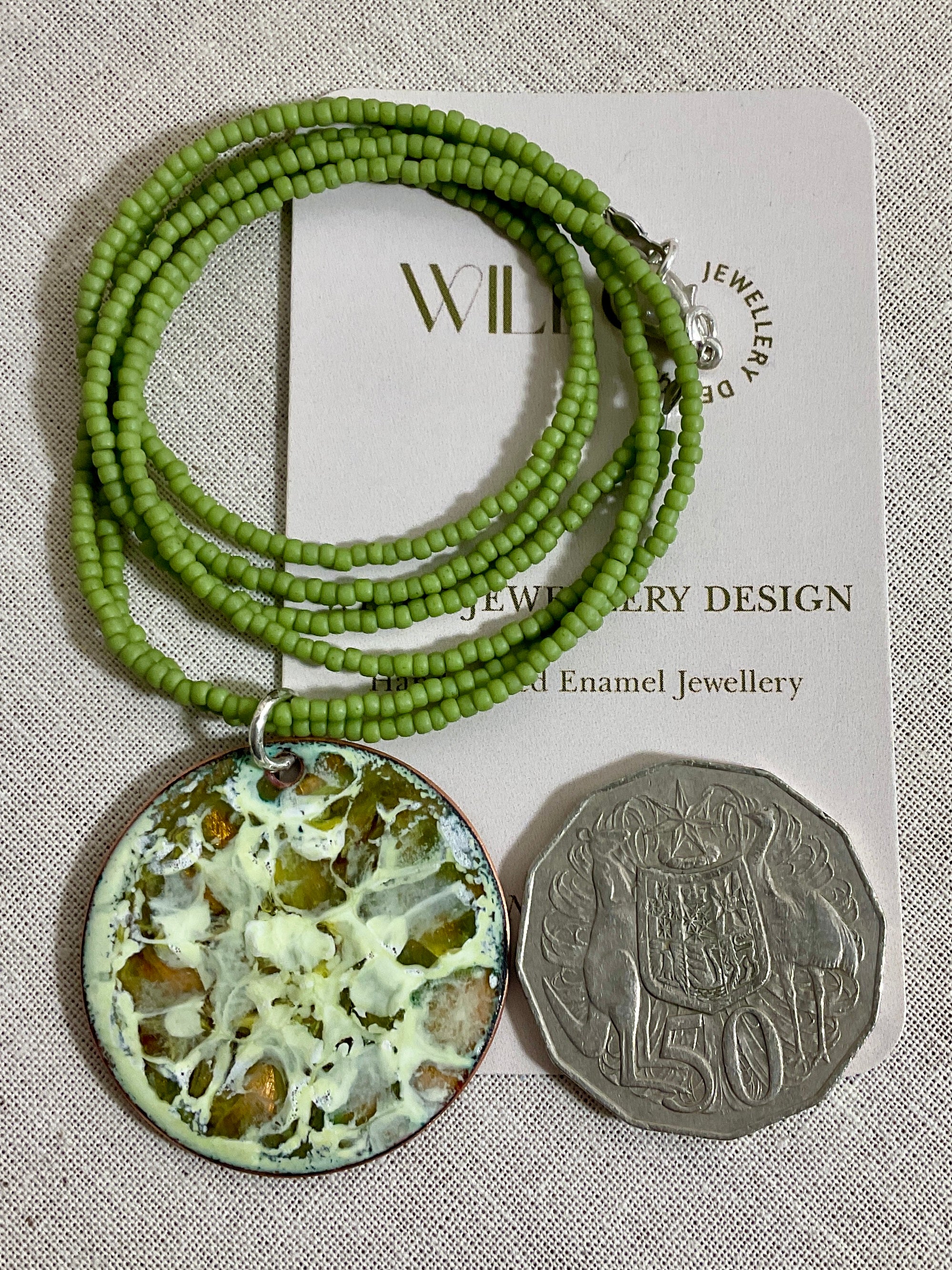 Yellow and green enamel pendant on green seed beads.