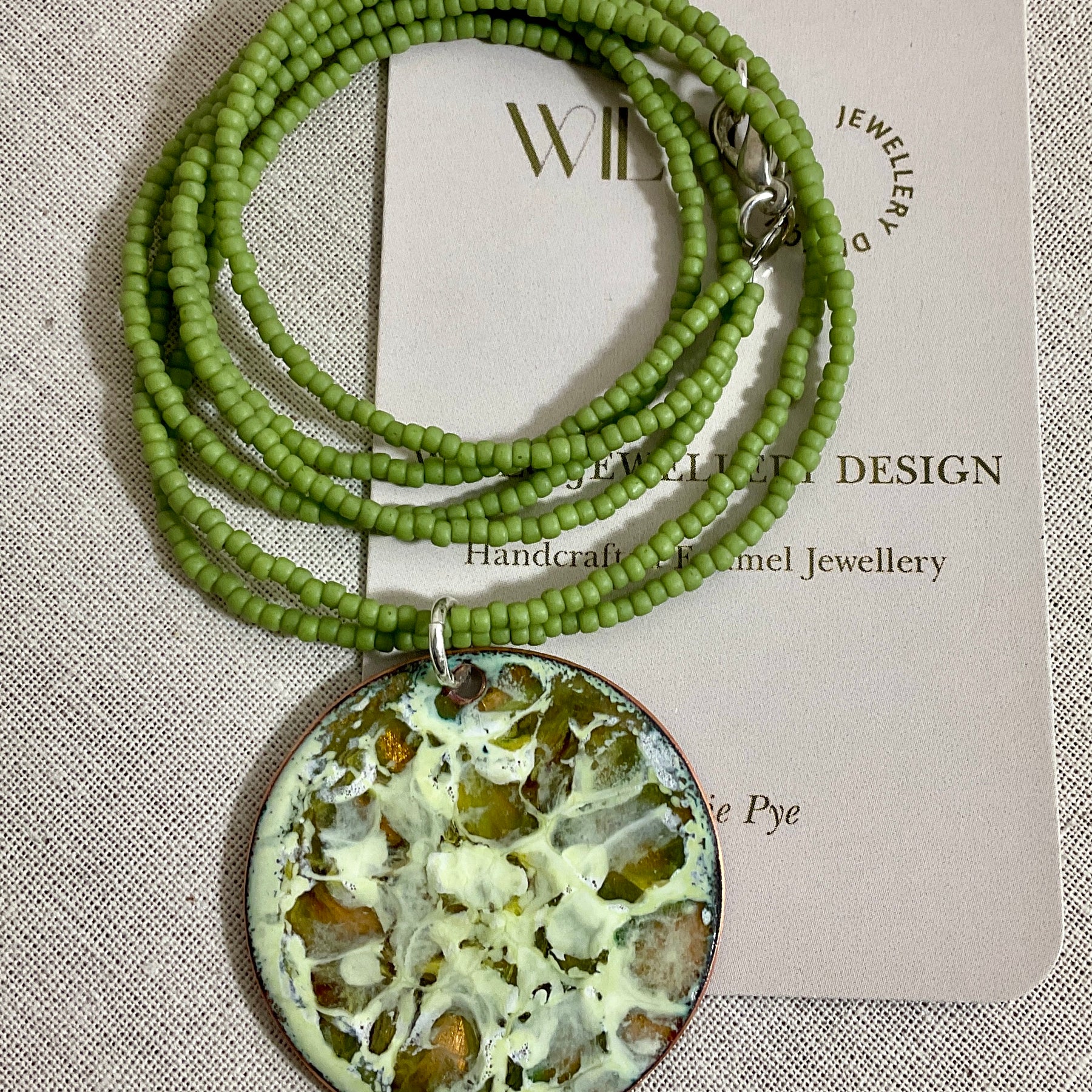 Yellow and green enamel pendant on green seed beads.