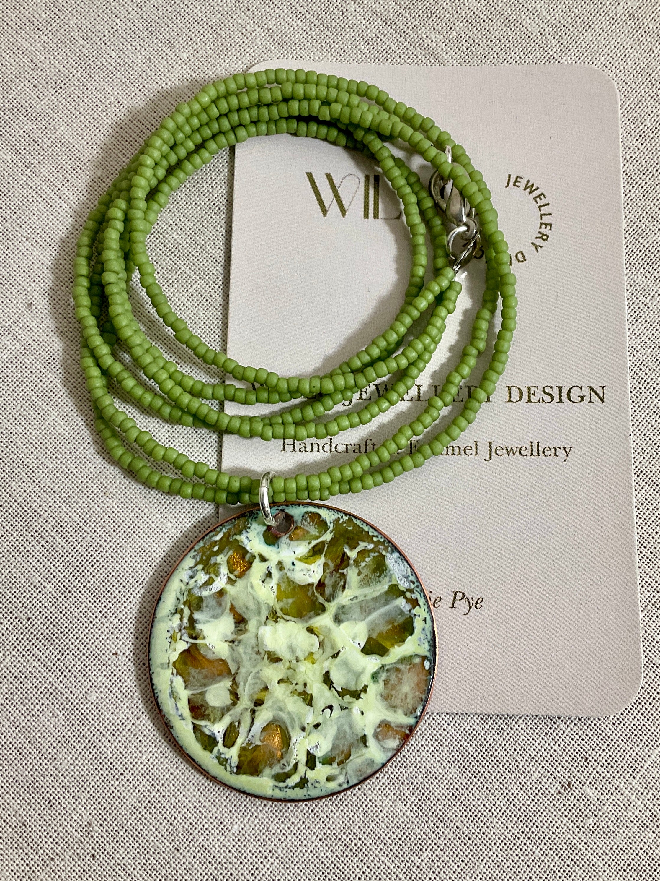 Yellow and green enamel pendant on green seed beads.