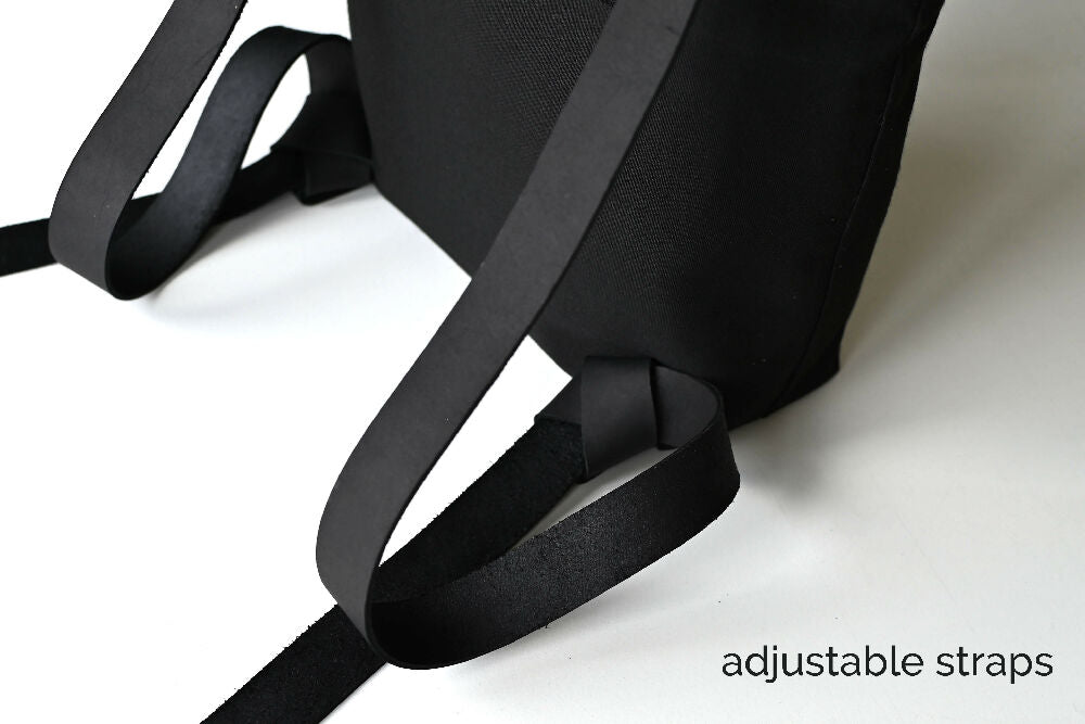 The adjustrable leather straps of a full black minimalist backpack.