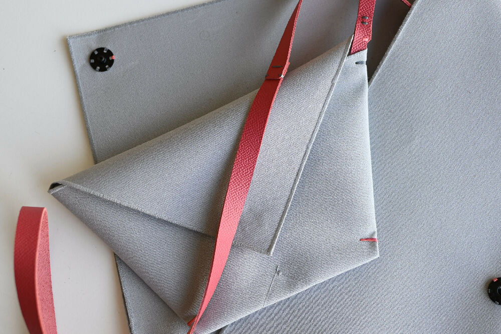 Minimalist gray envelope pochette is lying on a matching gray cluthc with salmon colour leather strap.