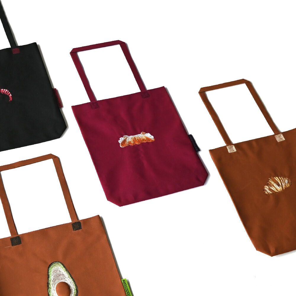four paperbag lookalike canvas tote bags with food embroidery in black, bordeaux and brown.