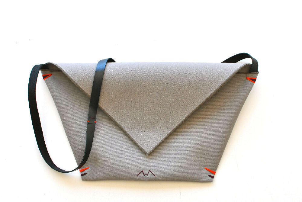 Gray minimalist envelope bag with black leather strap is lying on a white table.