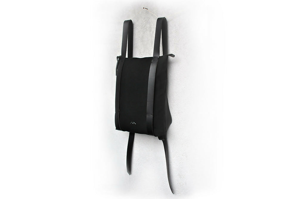 A full black backpack is hanging in front of a white wall