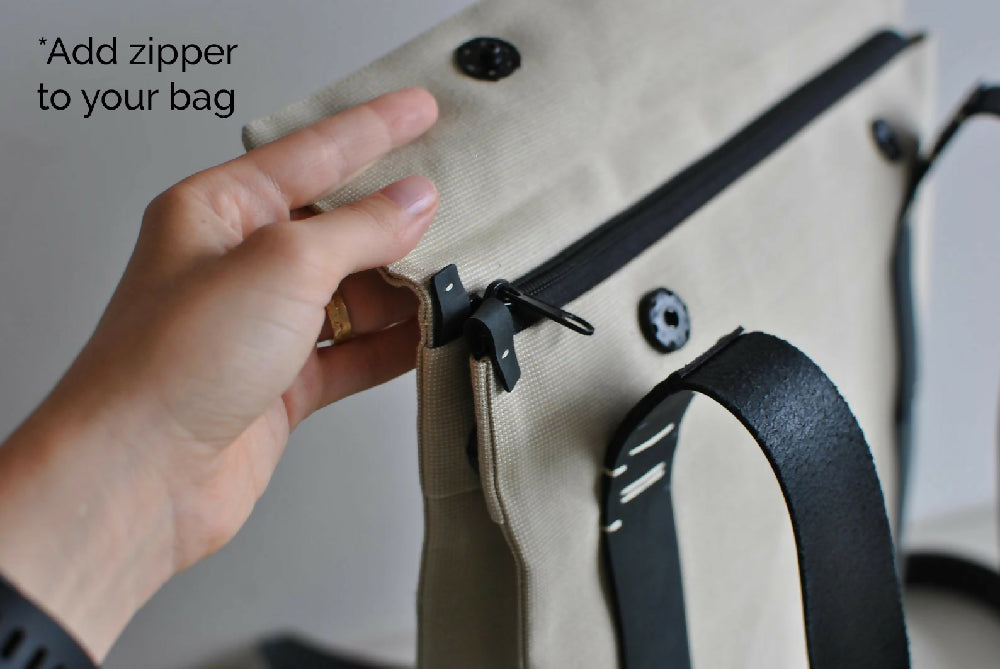 "Add zipper to you bag!" A hand is opening the flap of a beige backpak with black leather straps and black zipper and snap closure.
