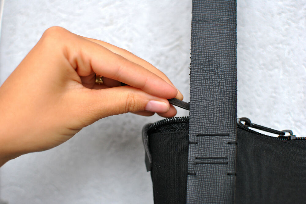 A hand is pulling a black zipper of a black backpack with leather straps to the left .