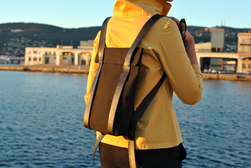 woman in a yellow blouse is standing in front of the sea and wearing a black minimalist backpack