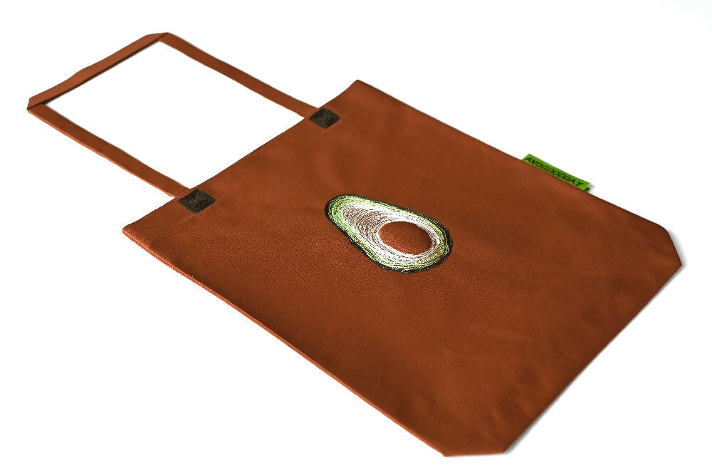 brown paperbag lookalike canvas tote with avocado embroidery on it lying on a white table.