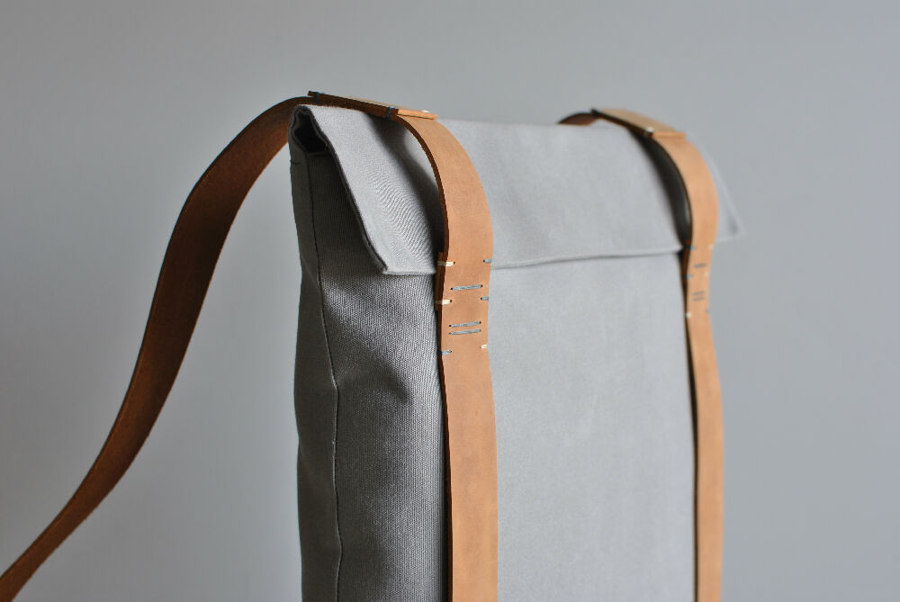 The upper part of a grey backpack with nude colour handstitched leather straps.