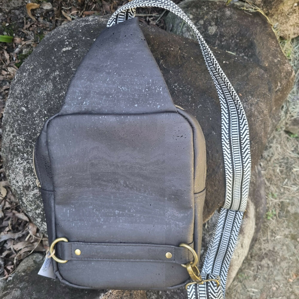 Black cork sling bag, rear view showing d-rings and decorative webbing.