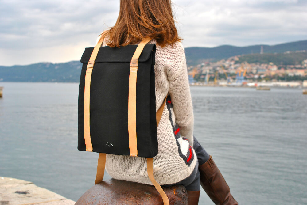 Woman with a black backpack with suede leather straps is sitting on a molo and watching the sea.