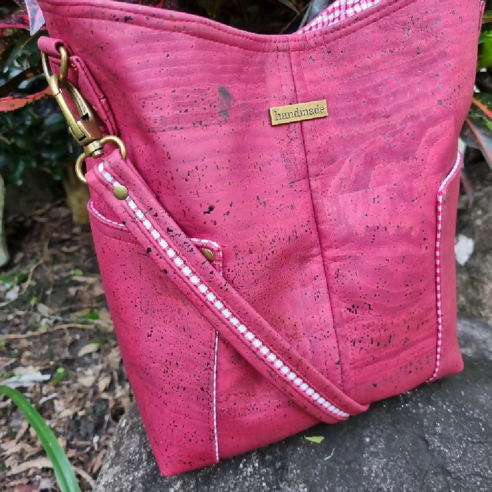 Women's shoulder bag in red wine coloured cork. It has a slip pocket on each side with a two-toned decorative shoulder strap.