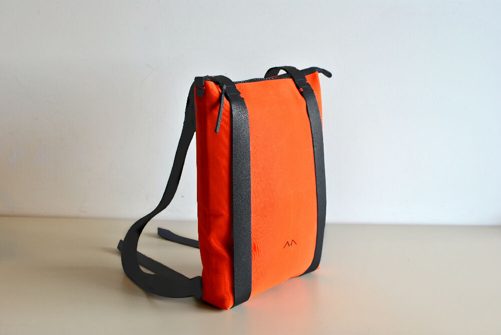 An orange canvas backpack with black leather straps is standing on a beige table.