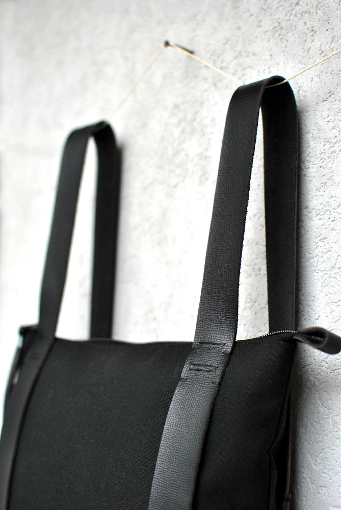 the upper side of a Black minimalist leather and canvas backpack