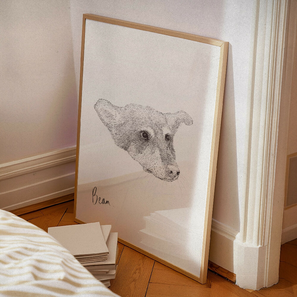 Framed custom pet portrait of a dog  leaning against a softly lit wall with stacked notebooks on a wooden floor. Aesthetic and minimalist home decor with a personalized artistic touch.