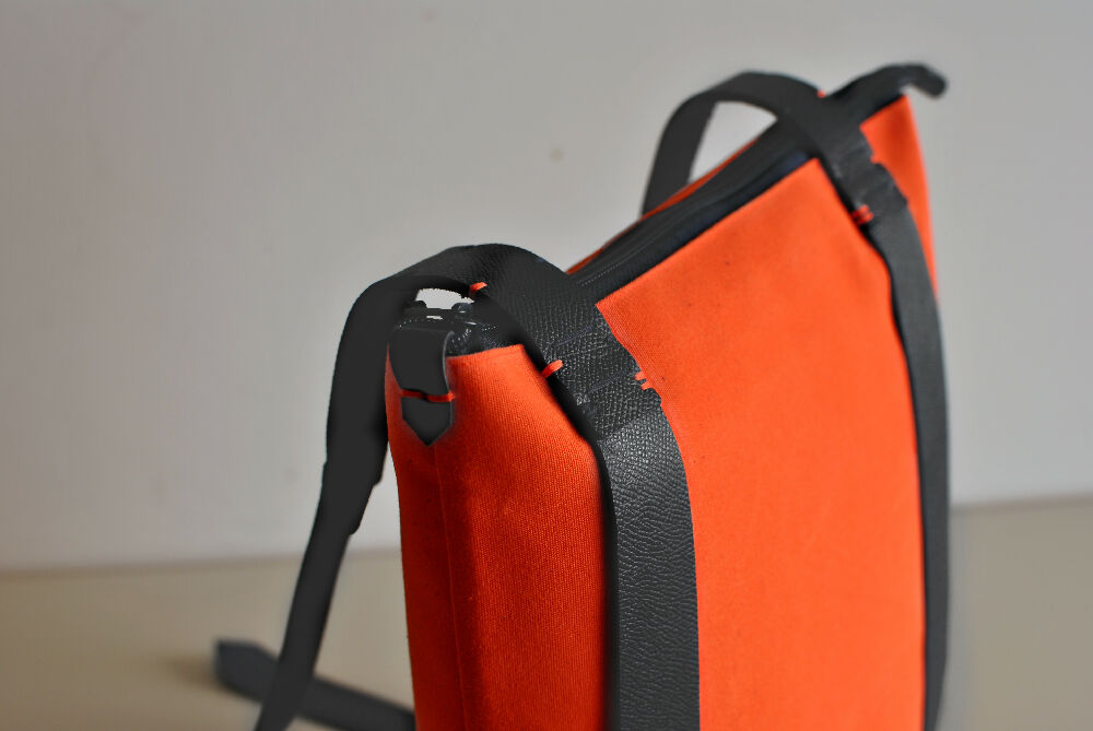 the upper side of an orange minimalist leather and canvas backpack