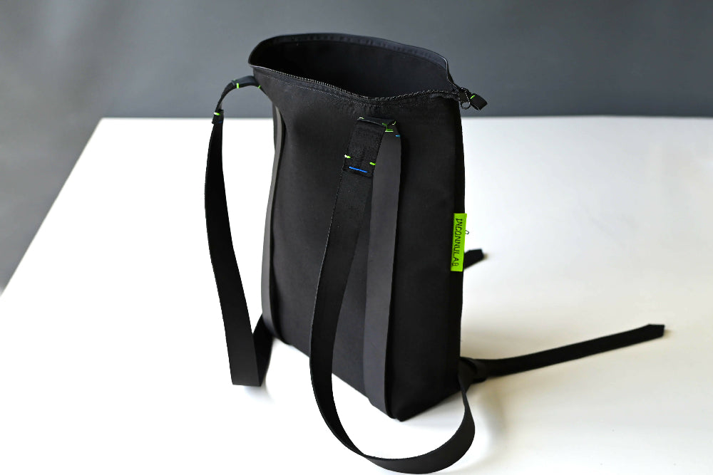 An open black zipper daypack is standing on a white table in front of a gray background.