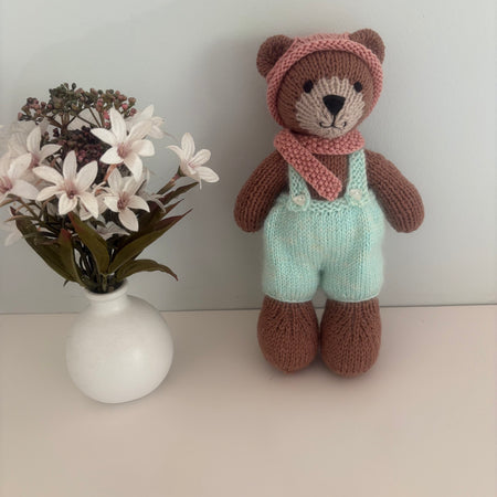 Little knitted bear in overalls, hat and scarf