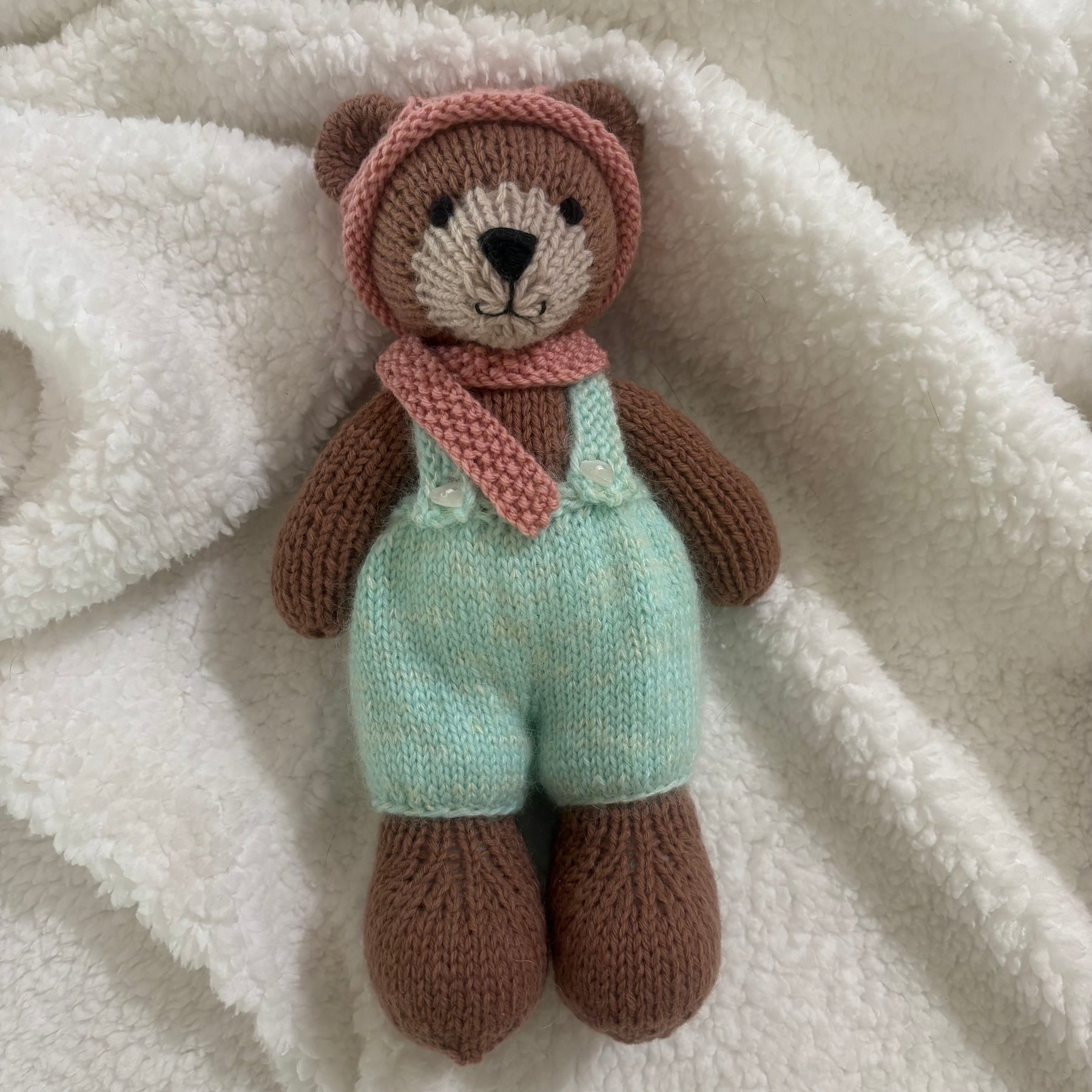 Little knitted bear in overalls, hat and scarf