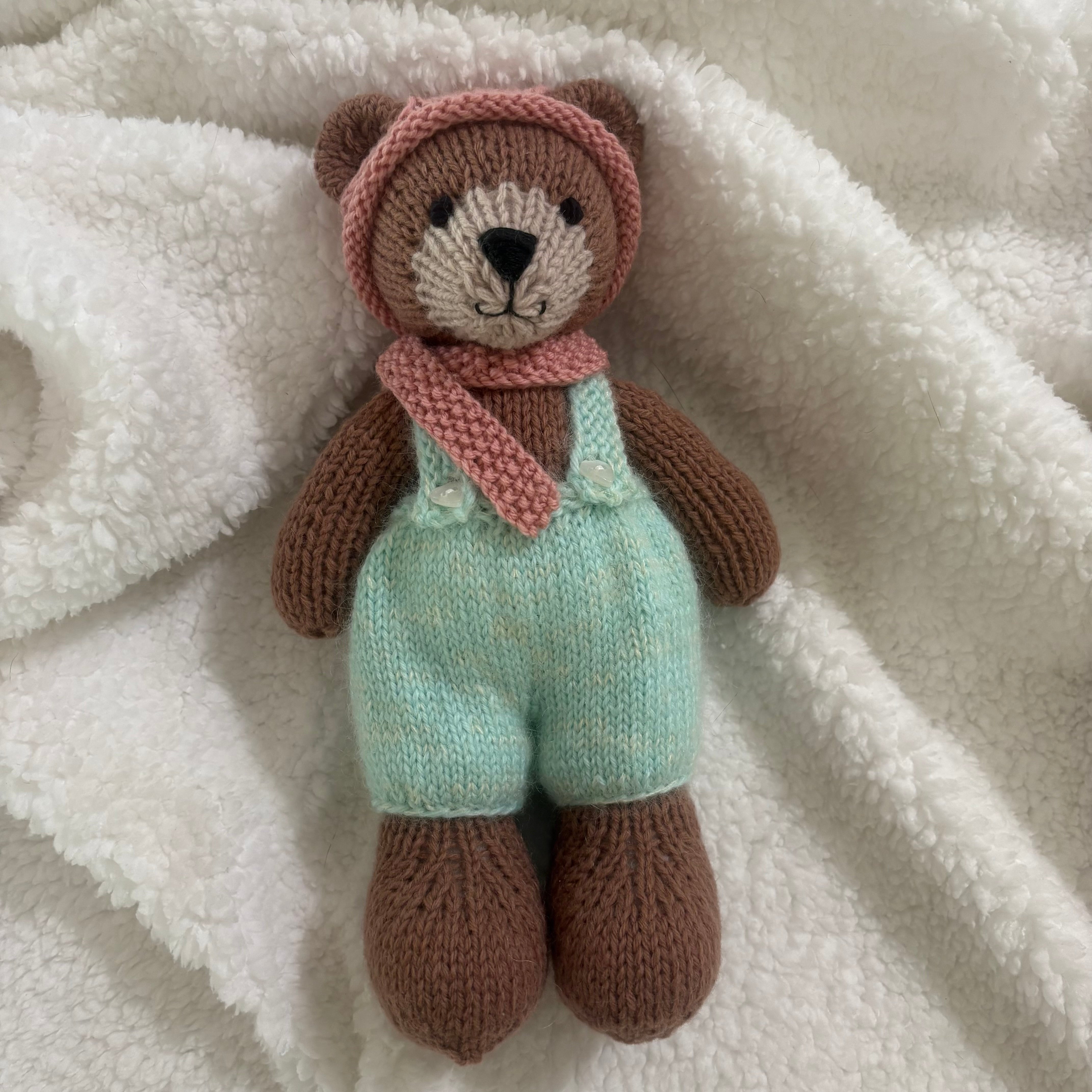 Little knitted bear in overalls, hat and scarf