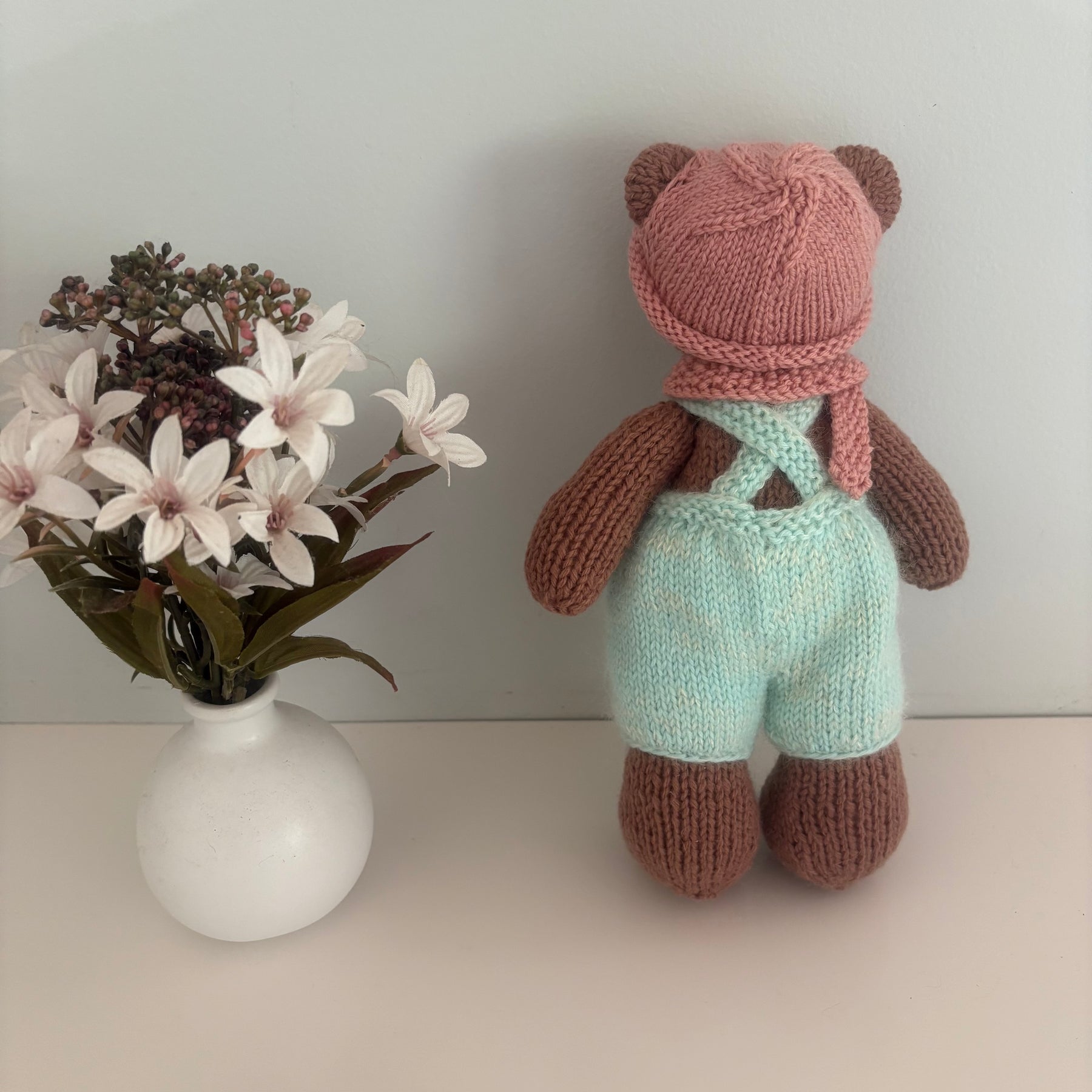 Little knitted bear in overalls, hat and scarf
