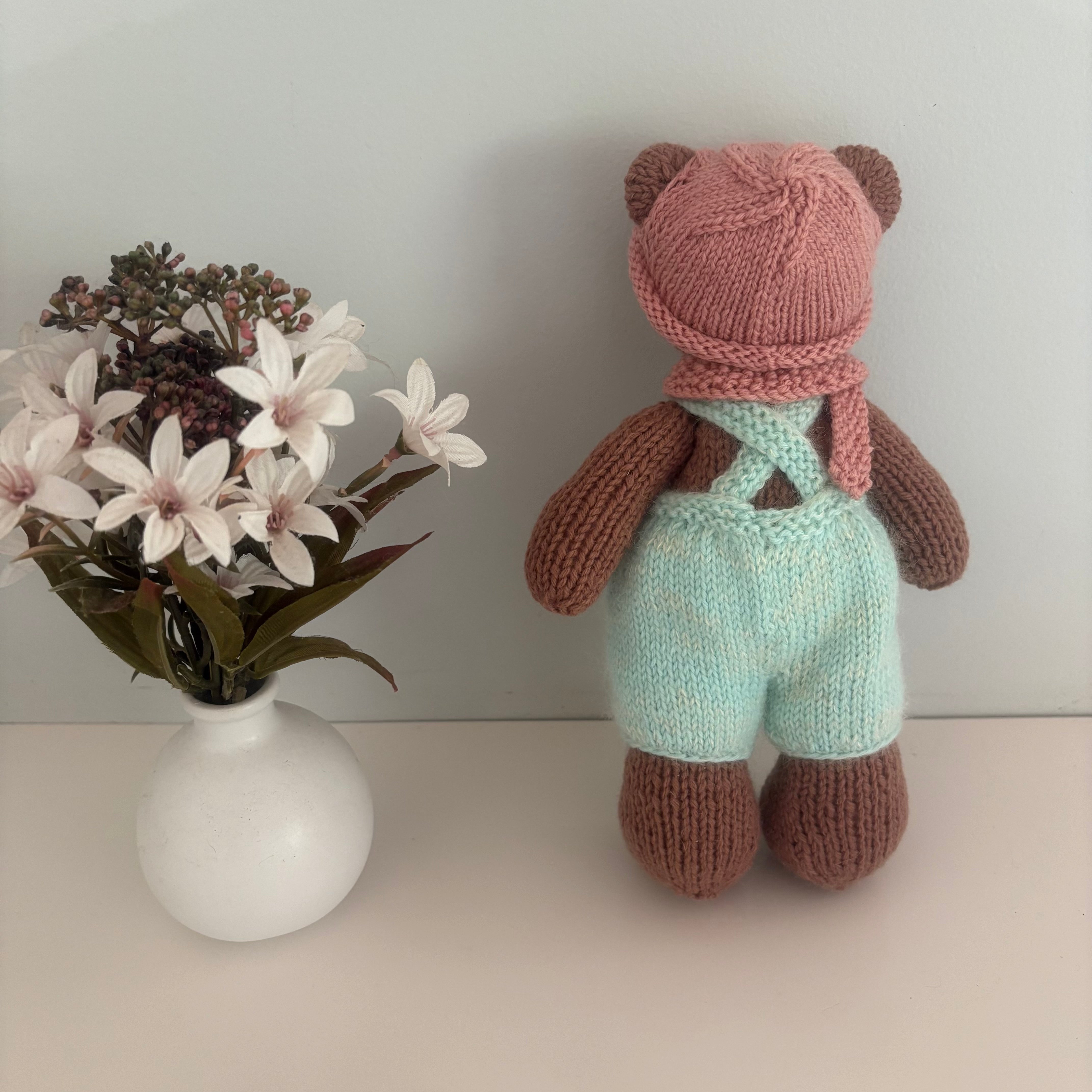 Little knitted bear in overalls, hat and scarf