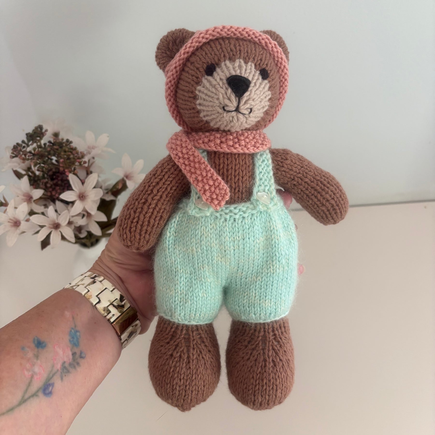 Little knitted bear in overalls, hat and scarf