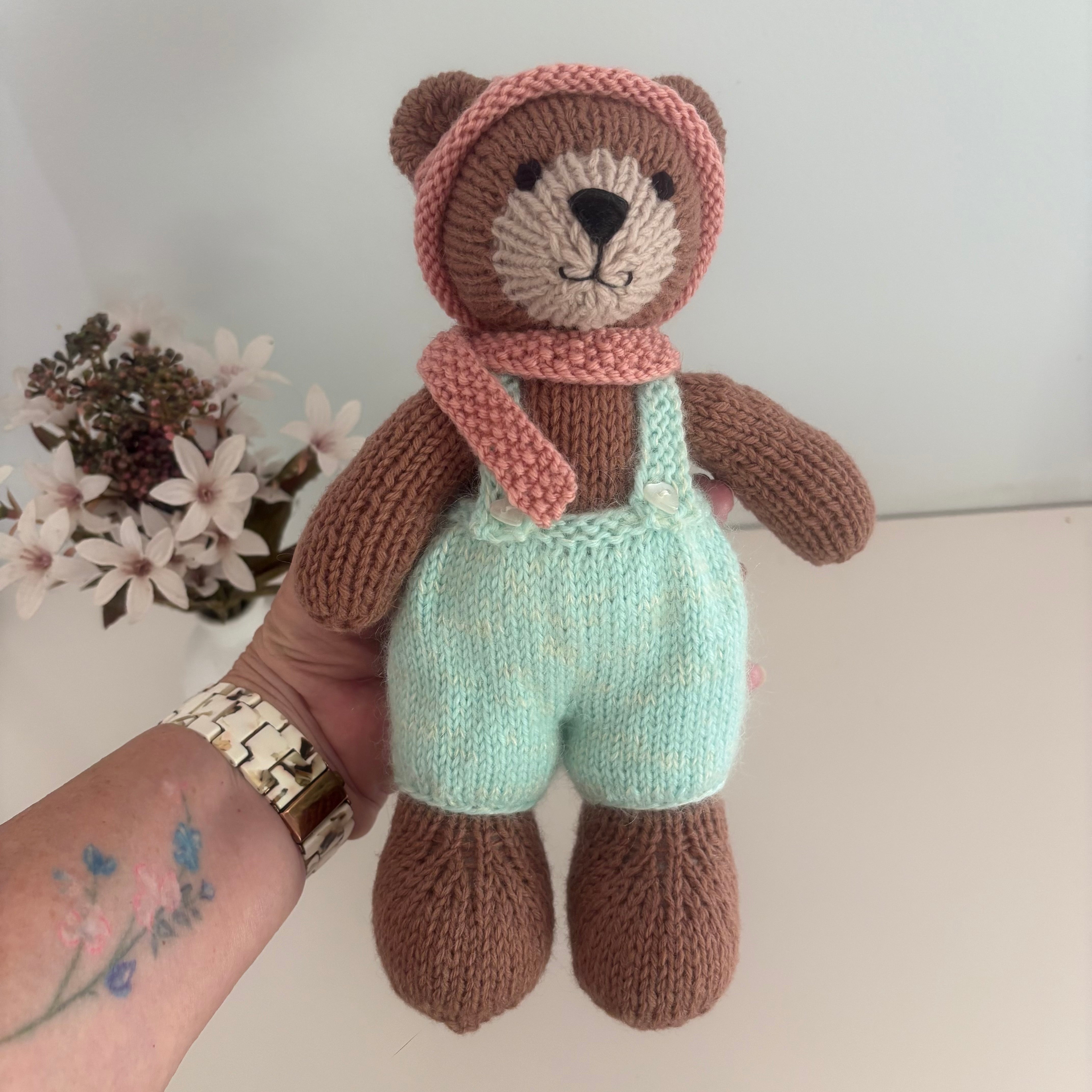 Little knitted bear in overalls, hat and scarf