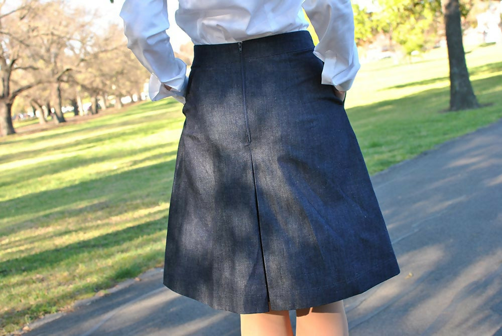The back side of a navy blue denim coulotte skirt worn by a woman in white shirt. Her hands are in the skirt's pockets.