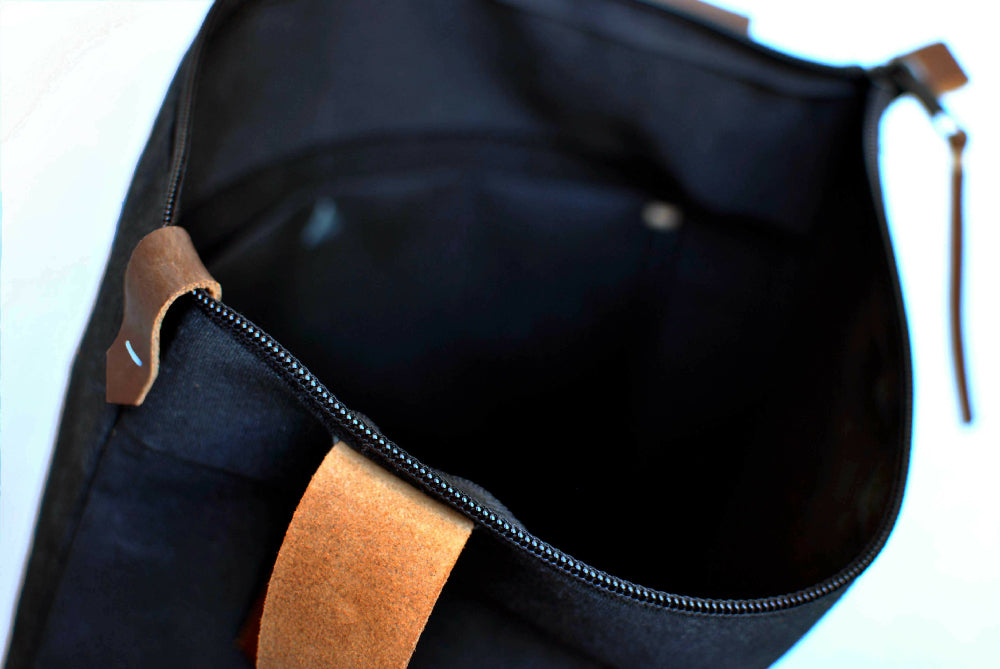 the inside of a black canvas bag with brown leather strap and zipper closure.