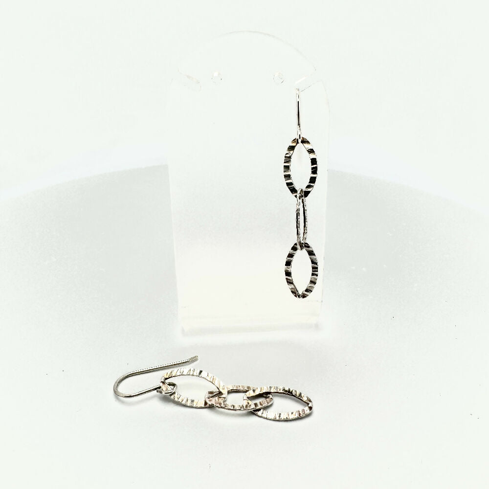 Textured sterling silver earrings one on stand and one laying down