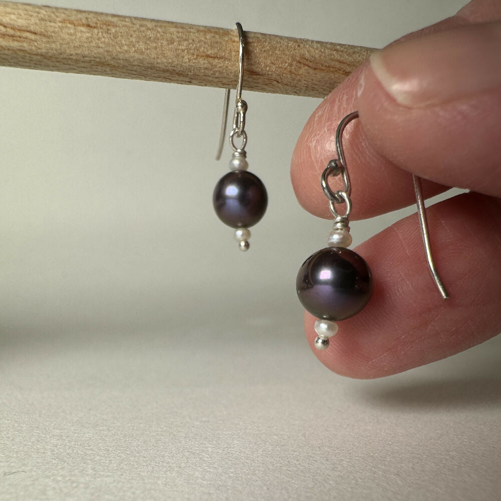 Large black pearl with 2 small white fresh water pearl earrings on white background one held in hand