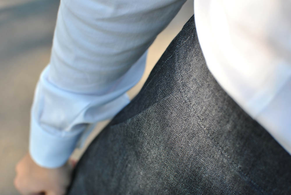 Details of adenim skirt. A woman is wearing it with white shirt. You can see the woman's righ hand.