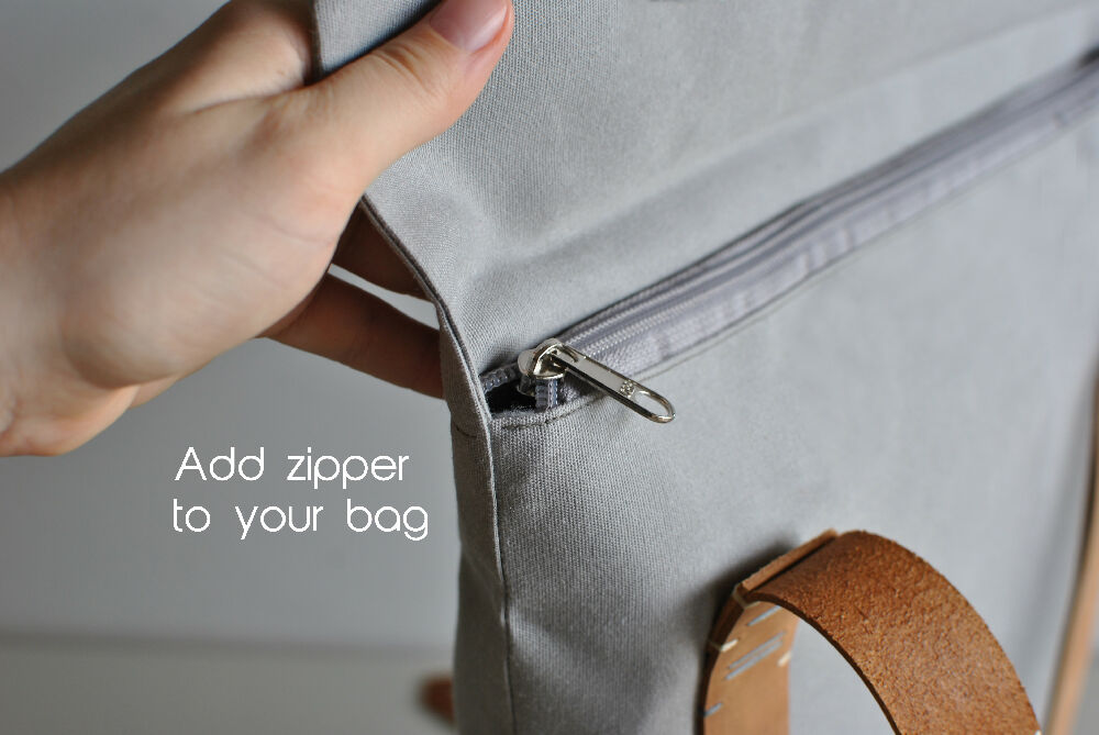 "Add zipper to your bag!" A hand is opening the flap of a gray canvas backpack with leather straps. The bag has a grey zipper.