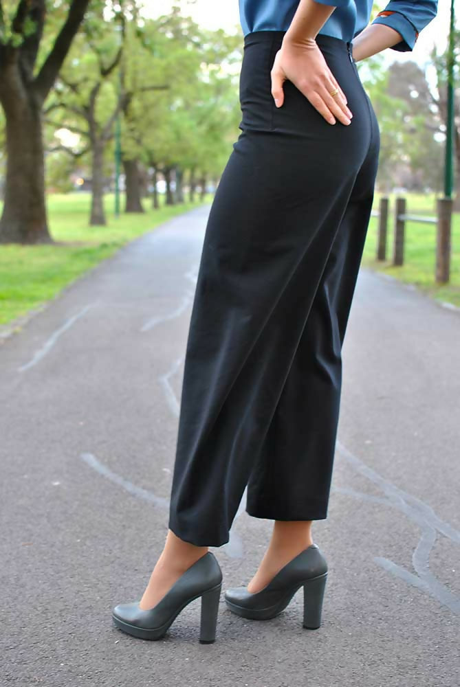 The lower part of a woman who is wearing black palazzo pants, blue blouse and gray high heel shoes. Her hands are on her hips.
