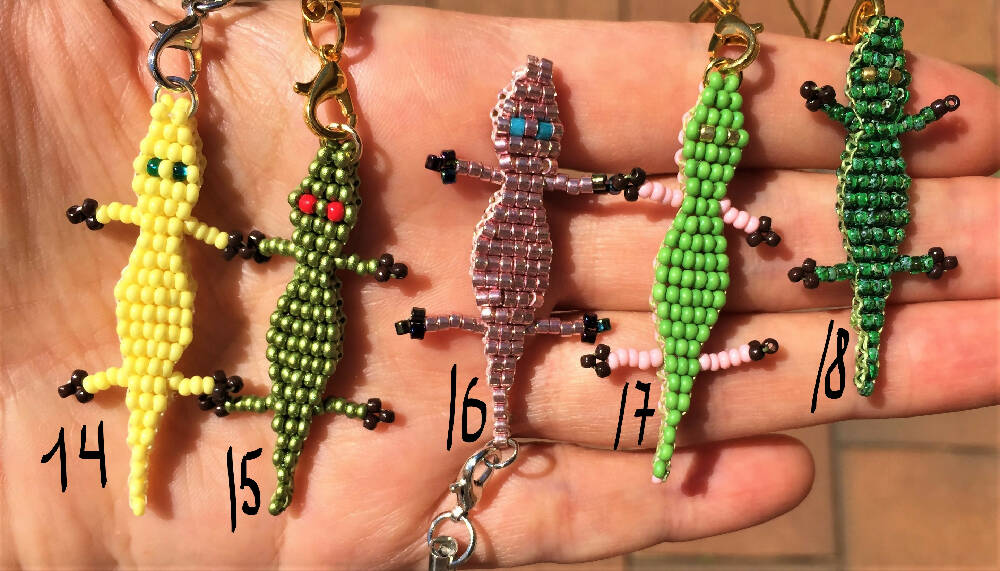 On the palm there are 5 Naryanabeads beaded croc with numbers.Number 14 next to yellow one, number 15 next to green one with red eyes, number 16 next to metallic pink one, number 17 next to double colour green/pink one, number 18 next to green one