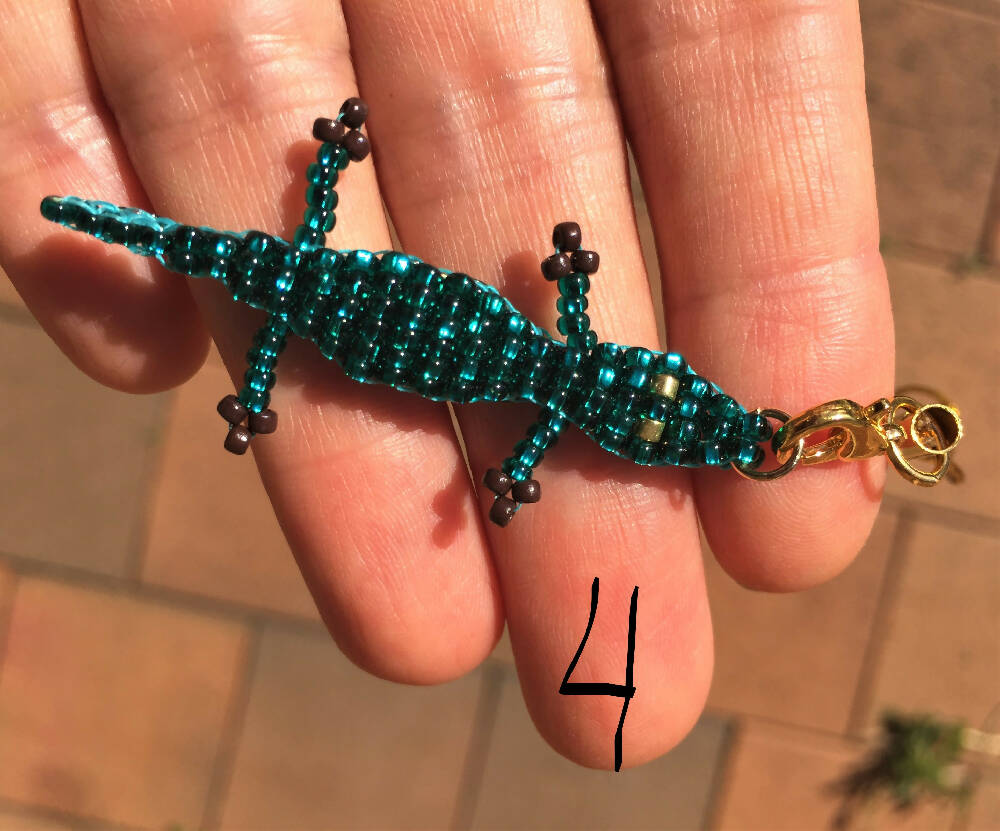 Fingers holding double layer shiny emerald crocodile. Body made of shiny emerald Preciosa seed beads, gold bead eyes, brown bead paws
