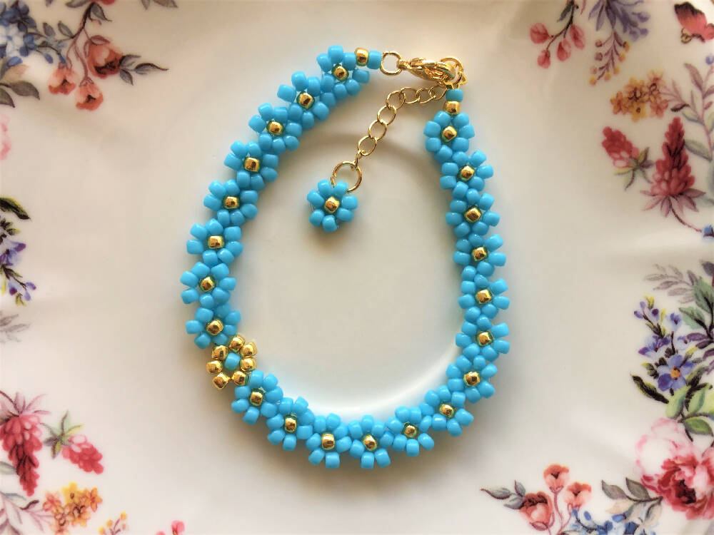 Naryanabeads light blue beaded bracelet made of light blue and golden colour seed beads. Clasp and extender chain - metallic gold colour, on the extender chain end light blue seed bead daisy flower
